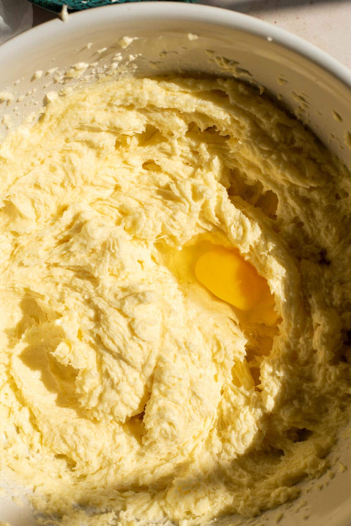 A mixing bowl full of beaten sugar, butter, and cream cheese with one egg yolk sitting in the middle.