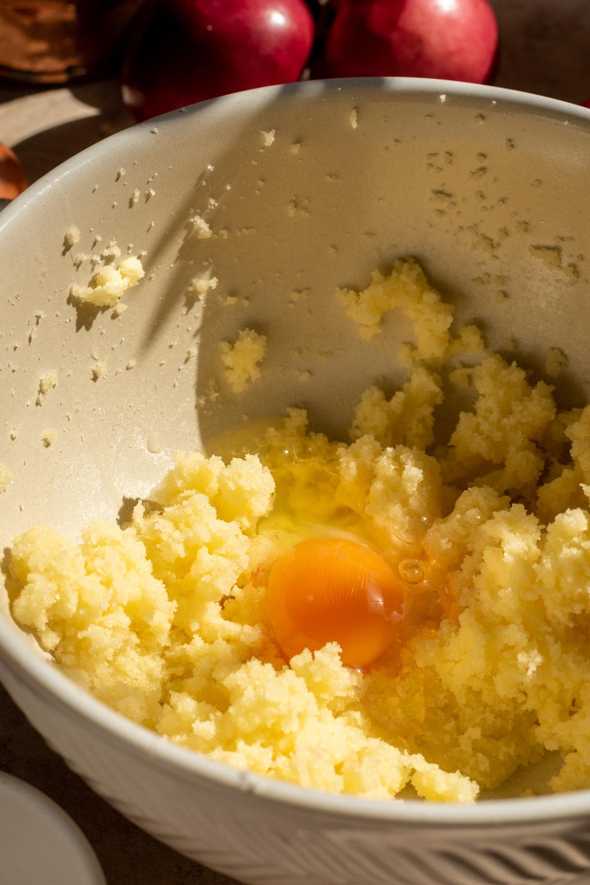 The butter and the sugar mixed in a cream bowl with one egg sitting in the mixture.