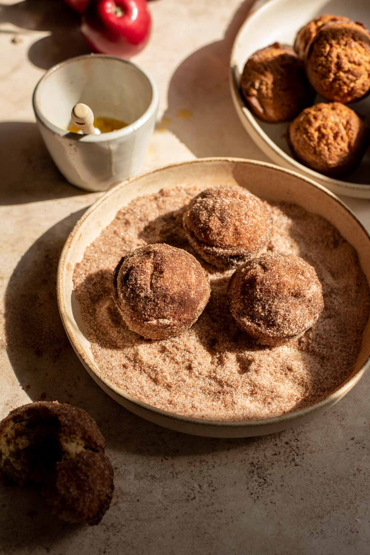 Baked muffins sitting in a bowl with cinnamon sugar.