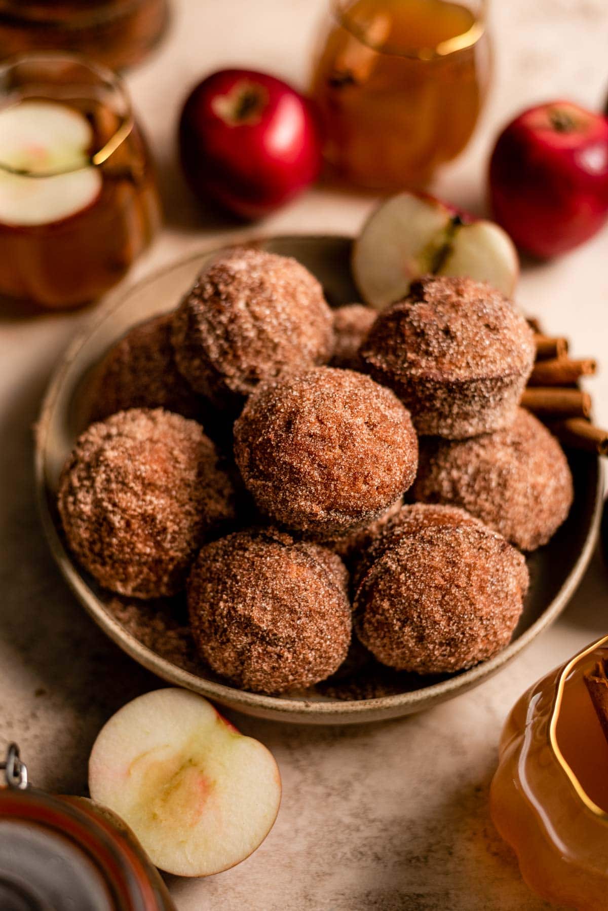 A bowl filled with apple cider muffins. sliced apple and cinnamon stick are surrounding the bowl.