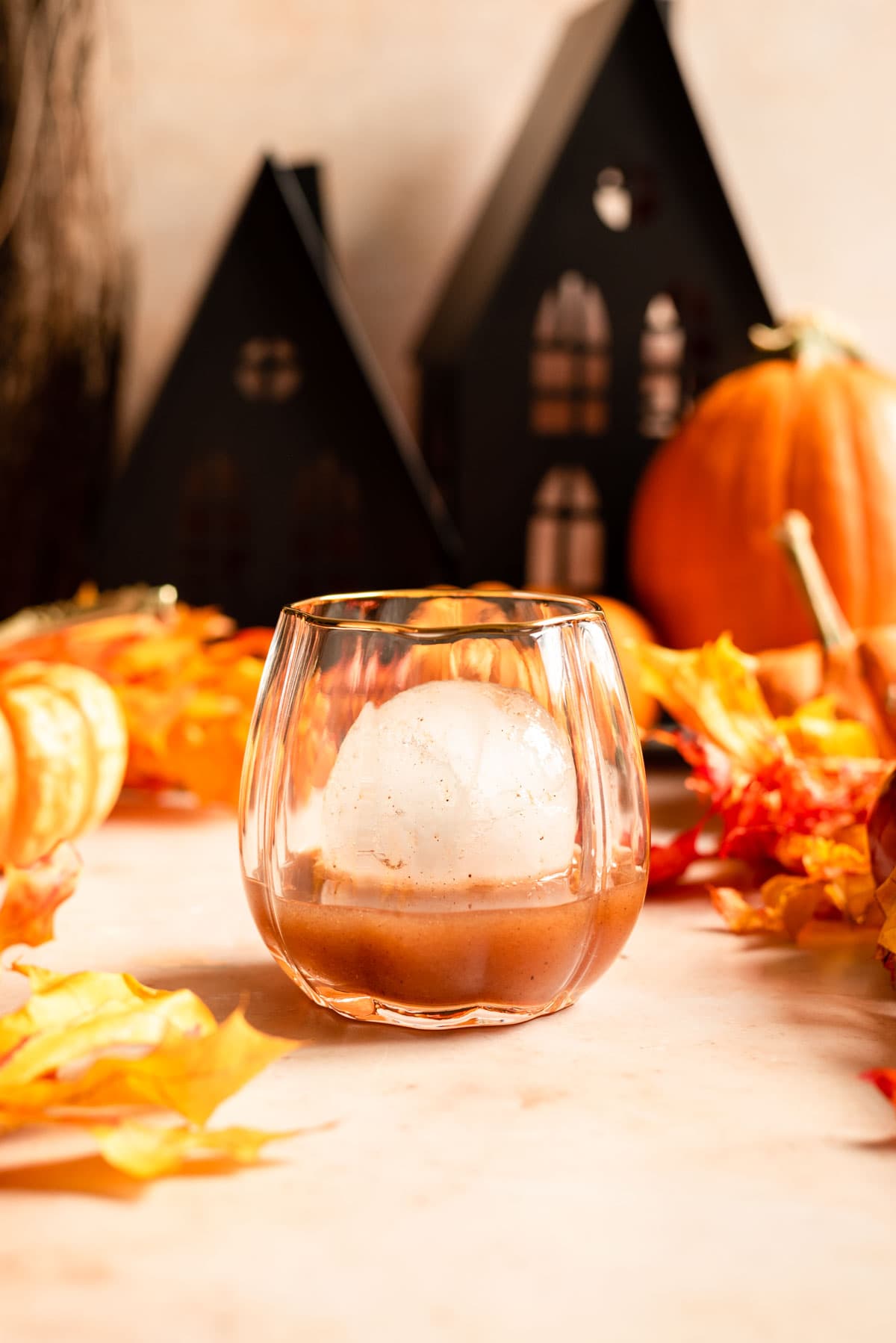 The bourbon mixture in a pumkin shaped glass with a large circle ice cube.