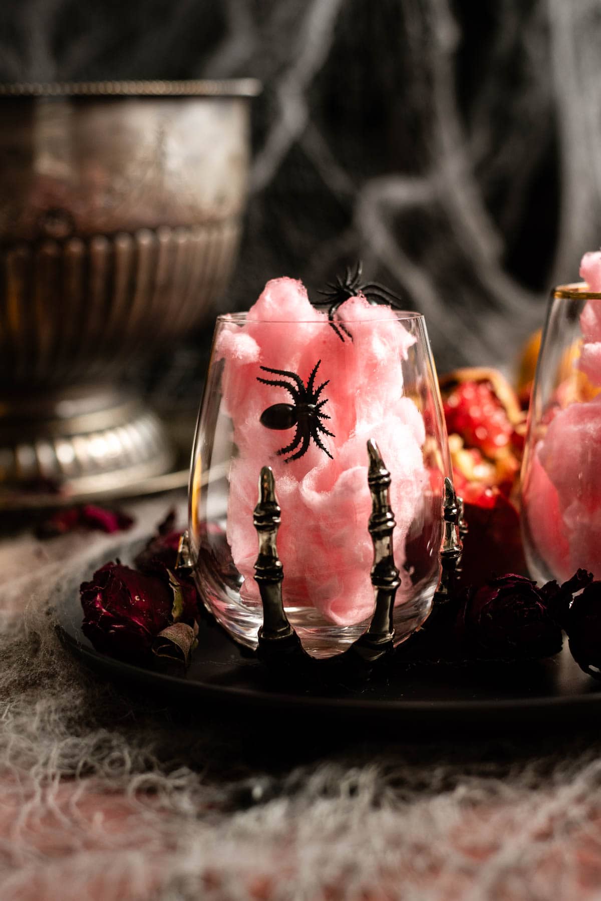 Skull hand wine glass filled with pink cotton candy and garnished with fake spider.