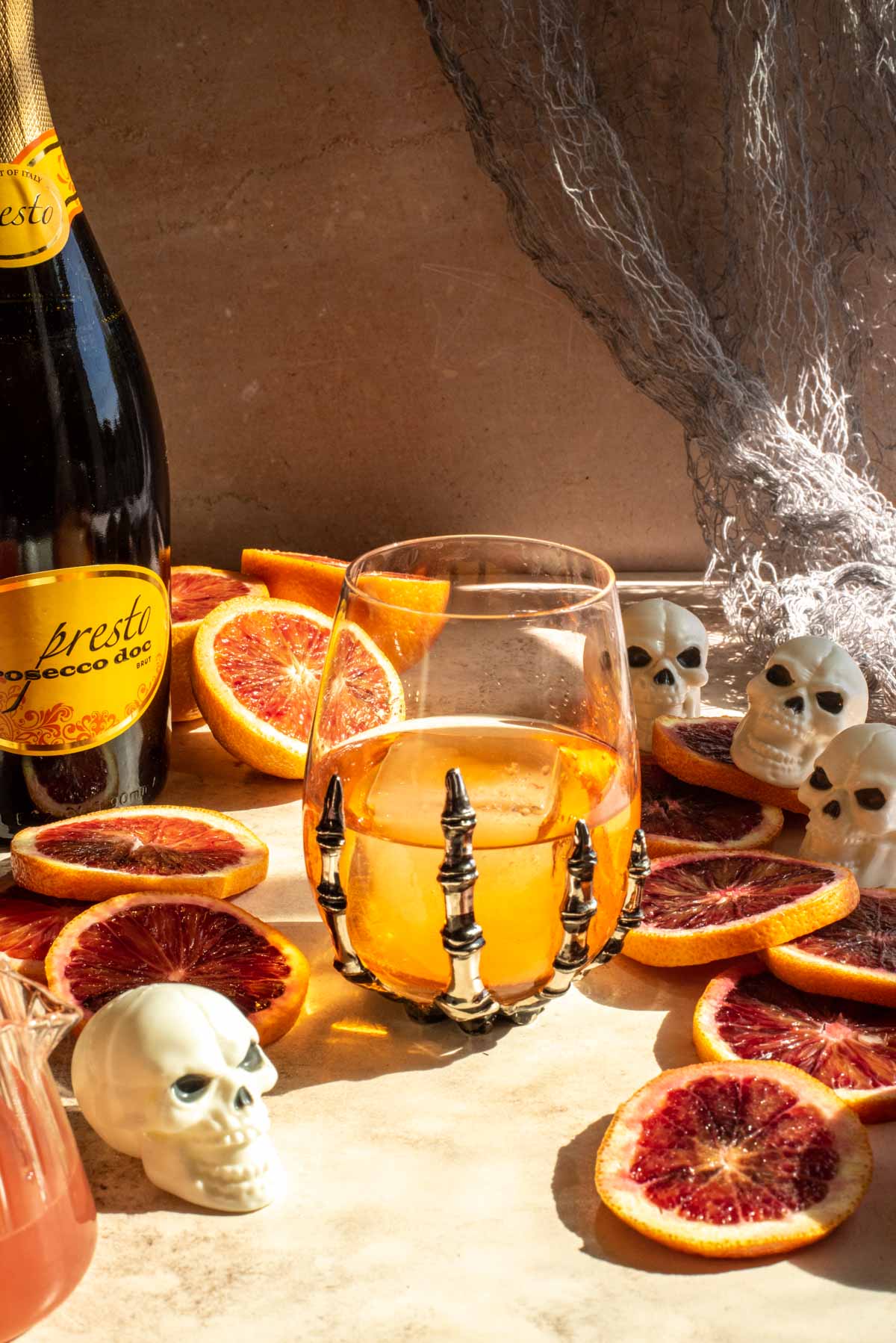 A skeleton hand wine glass with ice and aperol in it. It is also surrounded by blood orange slices.