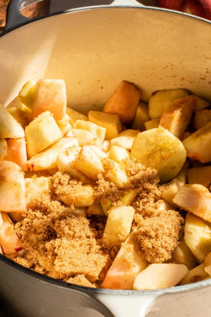 Peeled, cored, and sliced apples in a light brown dutch oven.