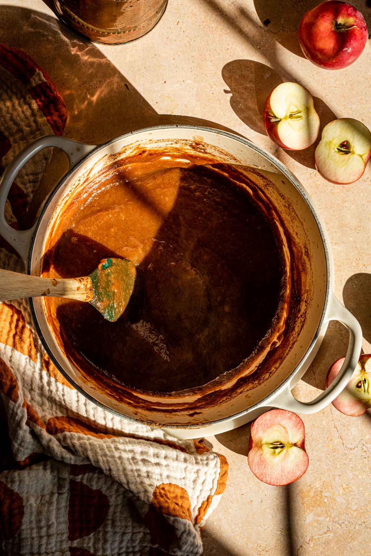 The cooked down apples in the dutch oven with a green spatula and apple slices off to the side.