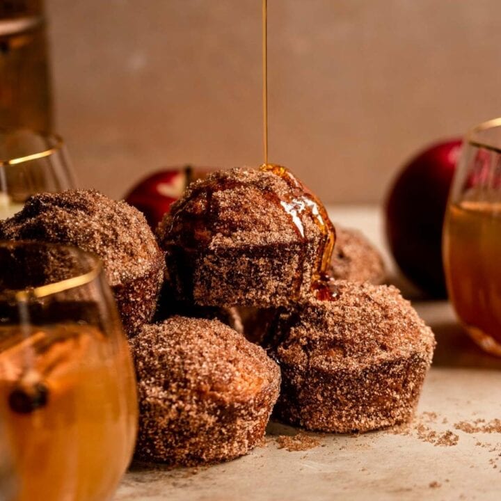 Apple cider muffins coated in cinnamon sugar with a maple syrup drizzle.