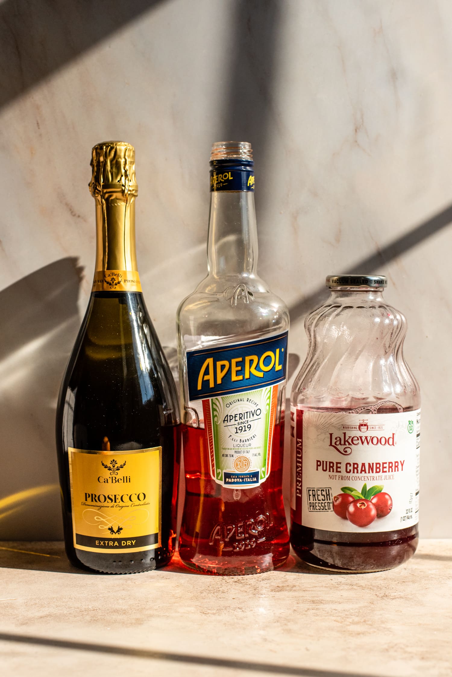 Ingredients for the cranberry aperol spritz against a marble wall.