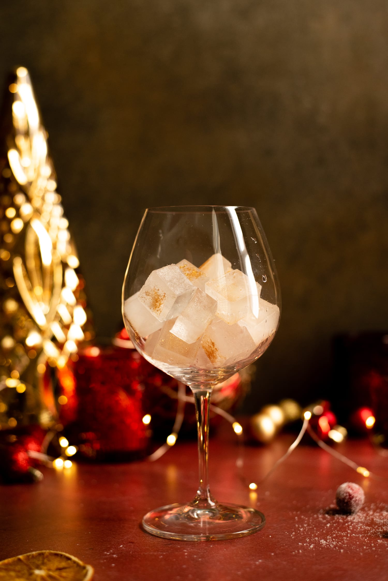 Gold glitter ice sitting in a large wine glass on a red table and surrounded by ornaments.
