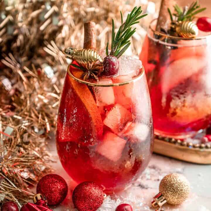 A cranberry aperol spritz garnished with rosemary, cinnamon, and cranberries.
