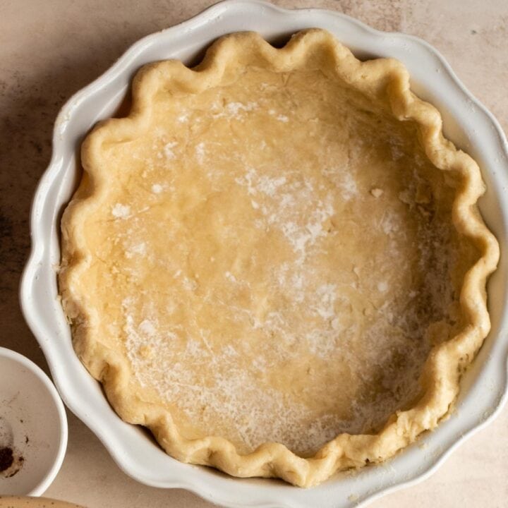 Crimped pie dough in a white pie pan.