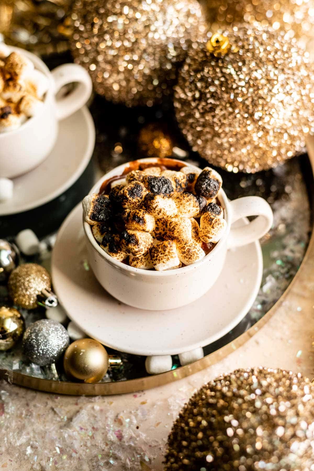 French hot chocolate topped with toasted marshmallows in a white mug with a saucer.