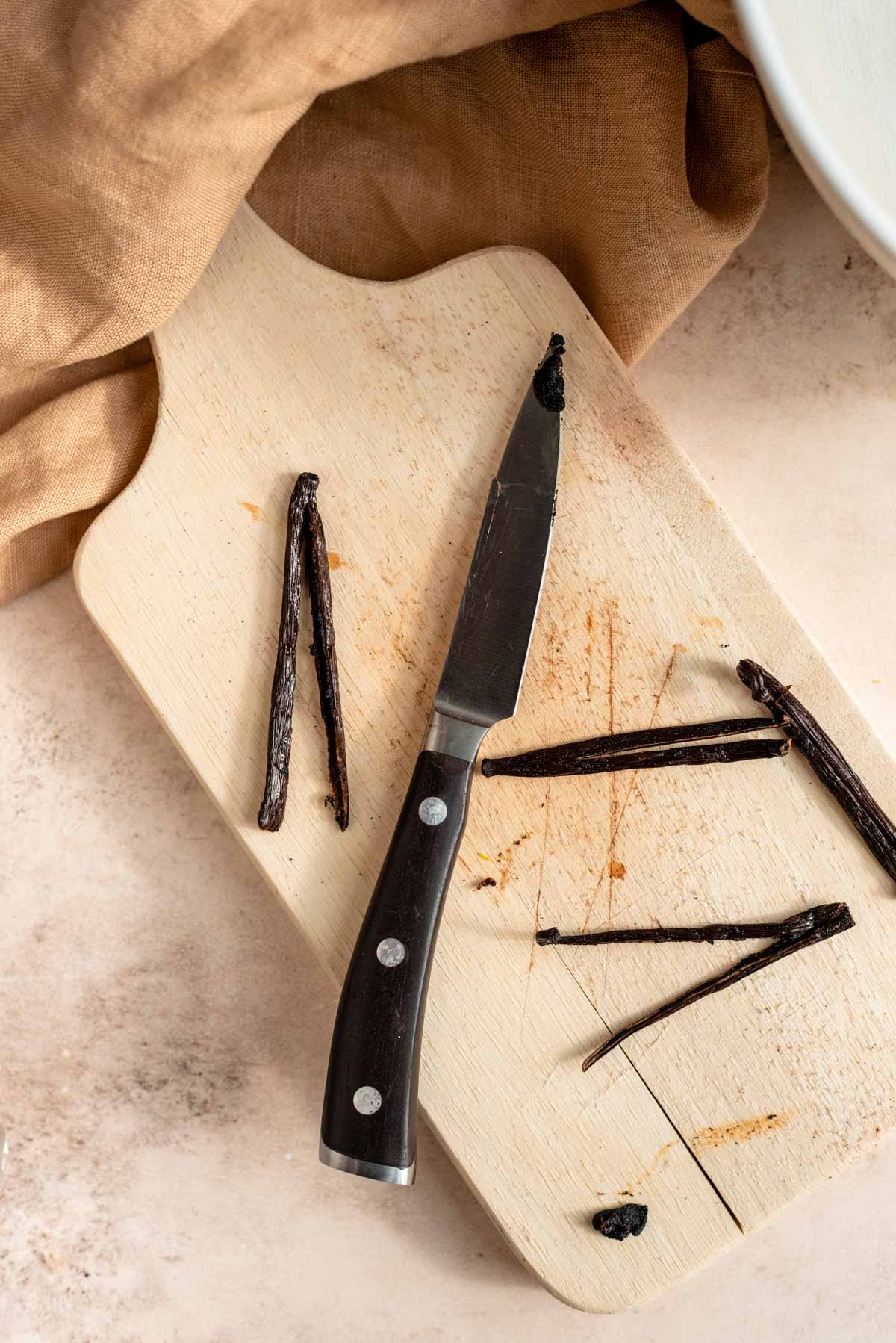 Sliced vanilla pods on a wood cutting board.