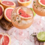 A pink coupe glass filled with the grapefruit mocktail and garnished with a grapefruit slice and thyme leaves.