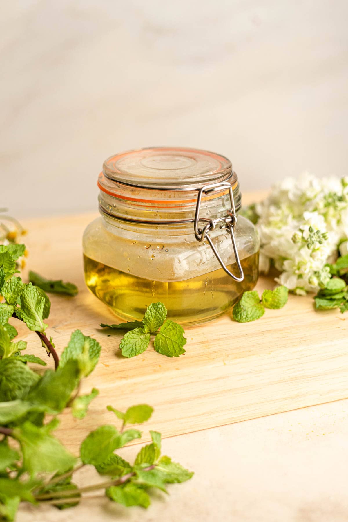 Mint simple syrup in a sealed jar surrounded by mint and white flowers.
