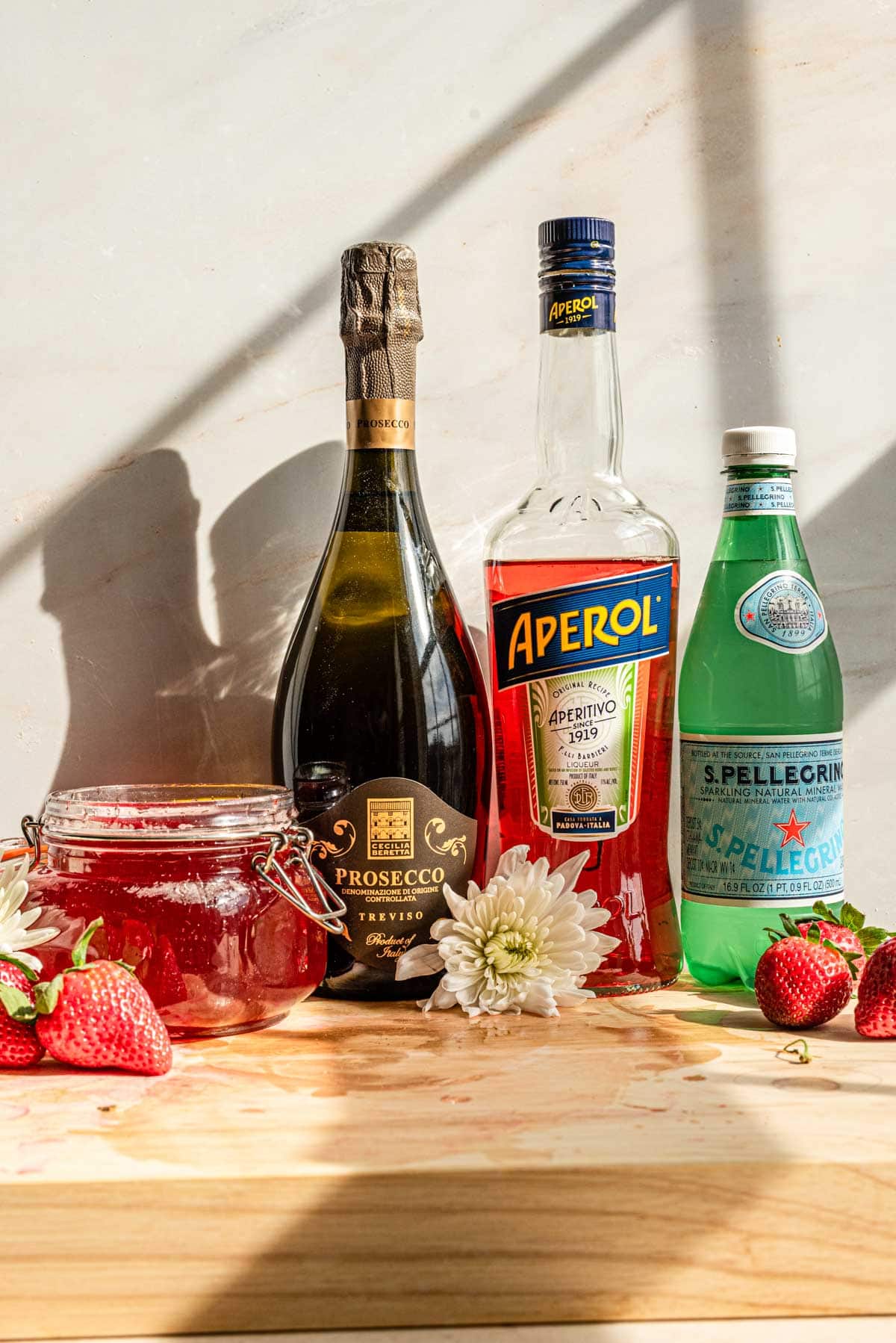 Ingredients for a strawberry aperol spritz on a brown table.