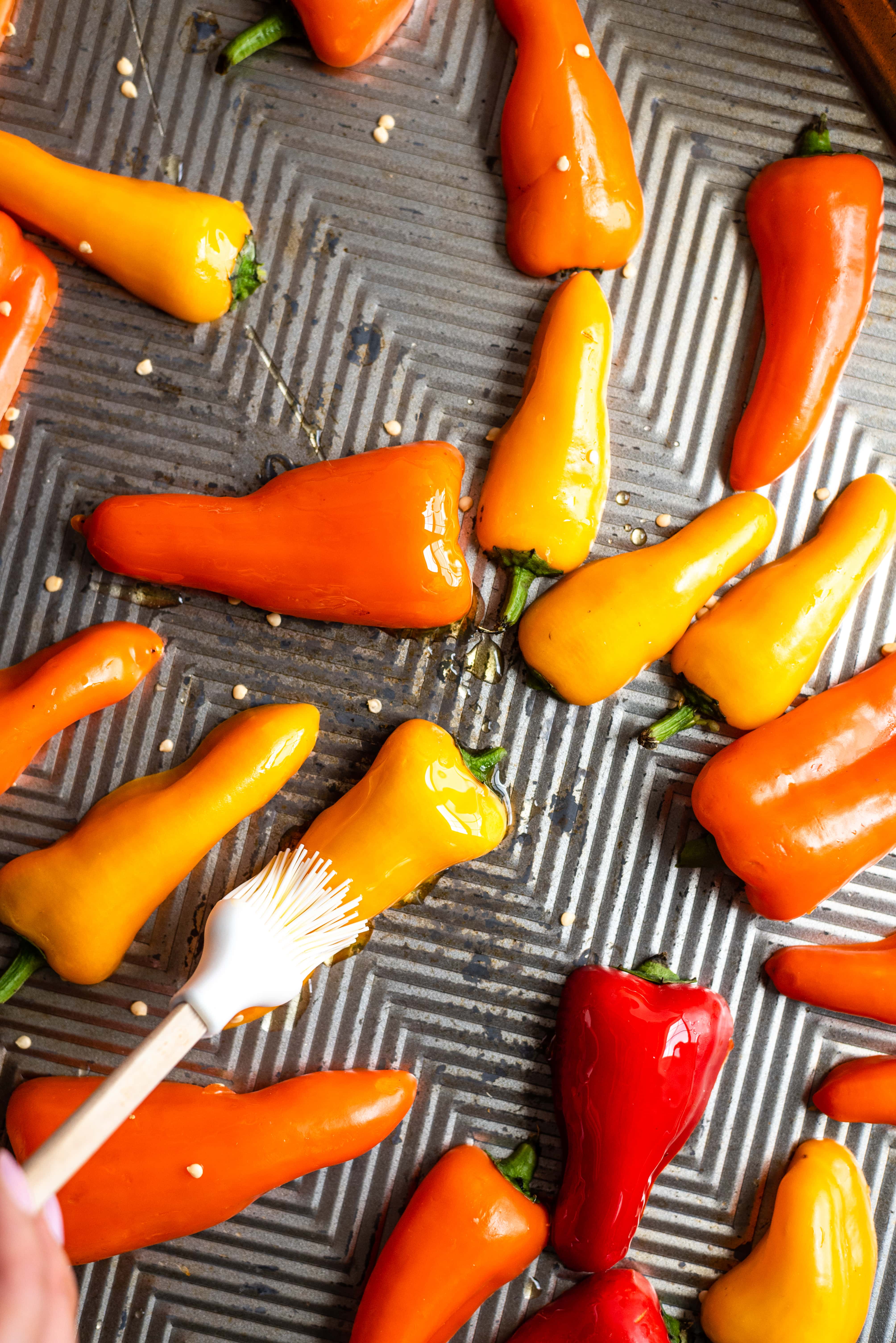 The sliced peppers being brushed with olive oil on a baking sheet,