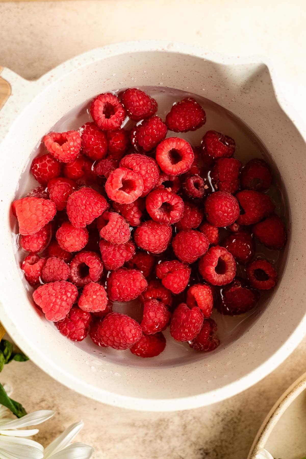 Raspberries, sugar, and water in a small white pot.