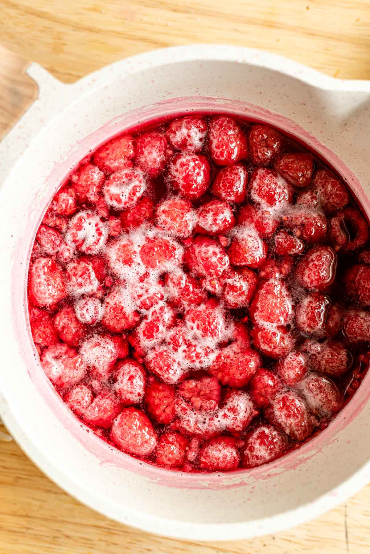 Simmered raspberry, sugar, and water in a small white pot.