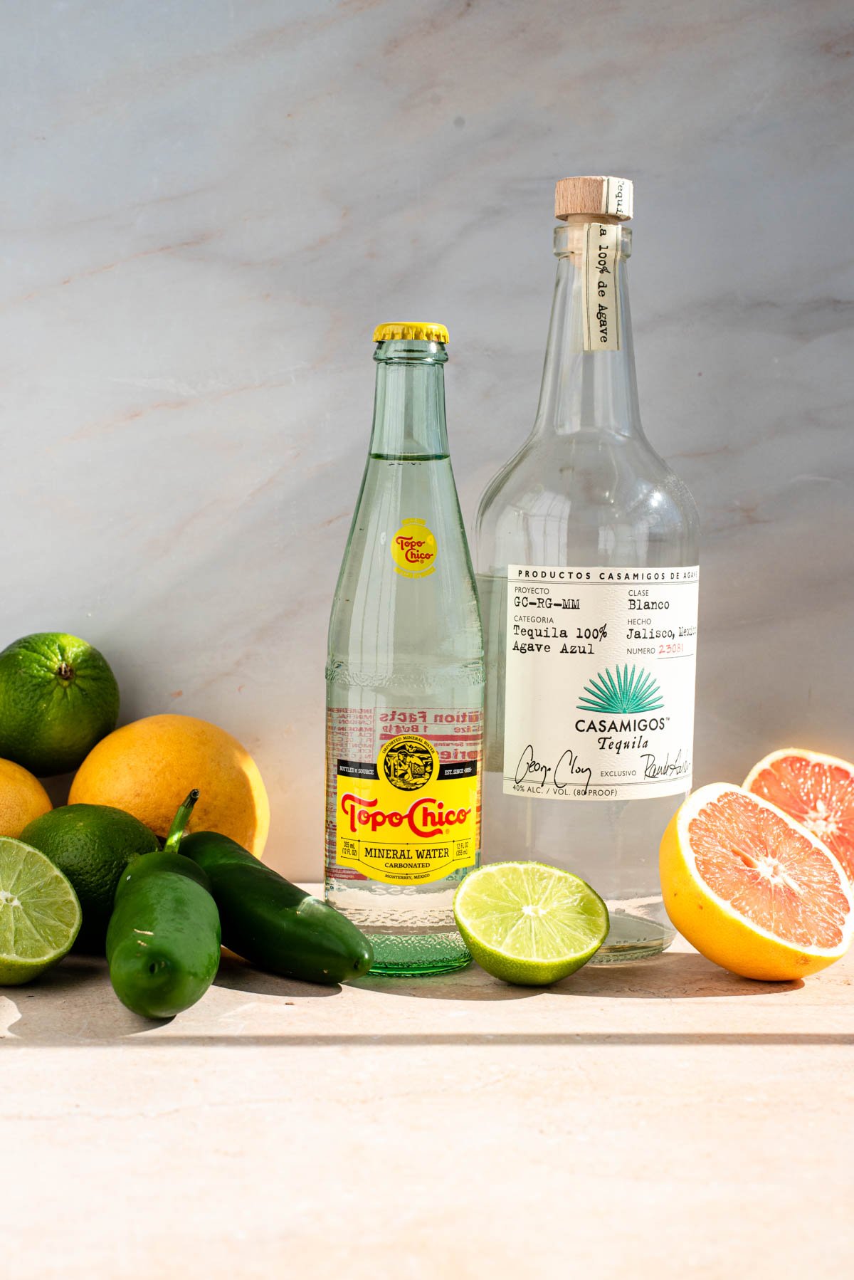 Tequila, Topo-Chico, grapefruit, lime, jalapeno on a brown table.