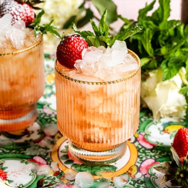 Strawberry mint julep in a clear textured glass with a dome of crushed ice and garnished with mint and a single strawberry.