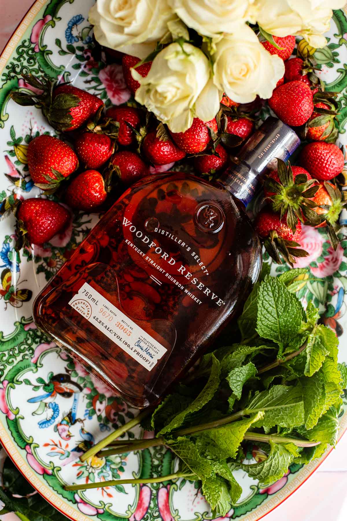 Strawberries, mint, and a handle of Woodford Reserve bourbon on a pink and green serving platter.