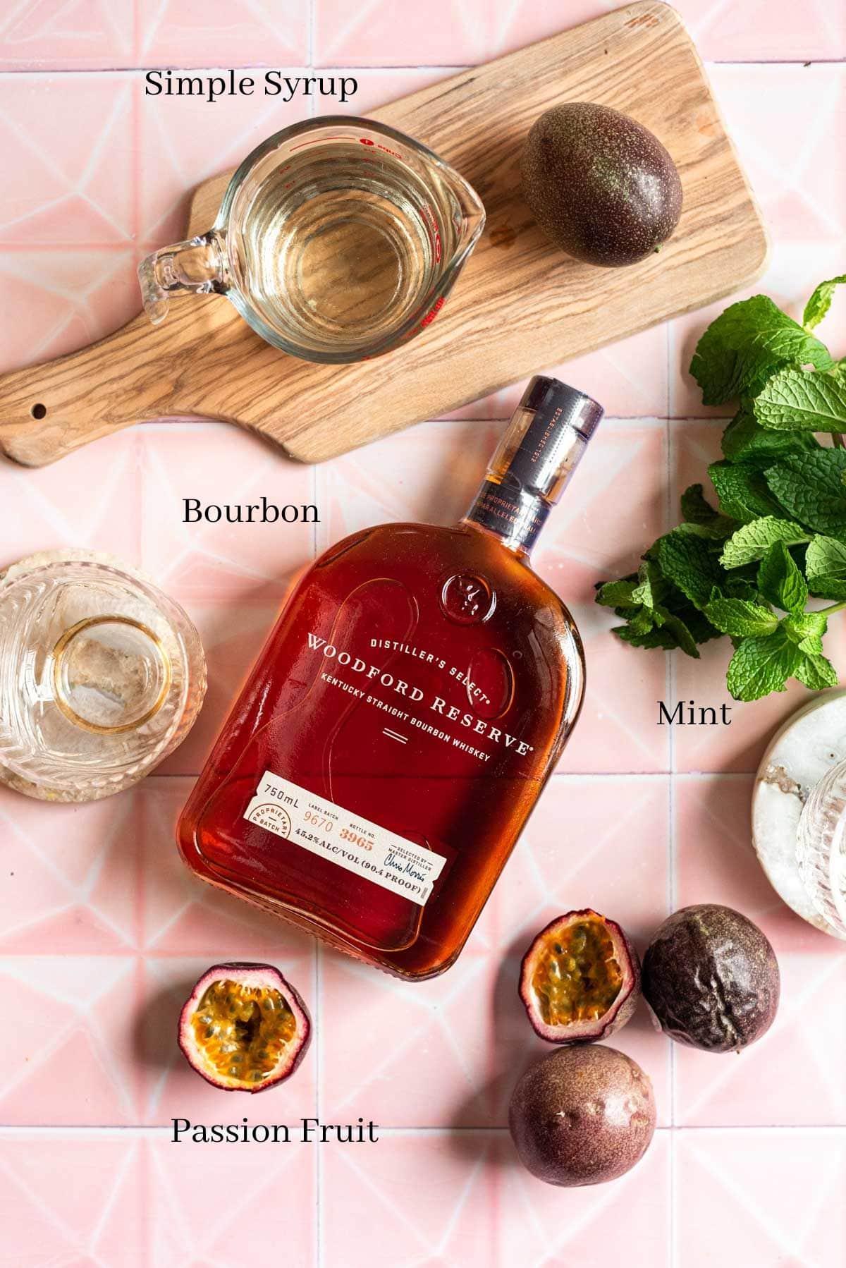 A bottle of Woodford Reserve bourbon surrounded by pass fruits, simple syrup and mint.