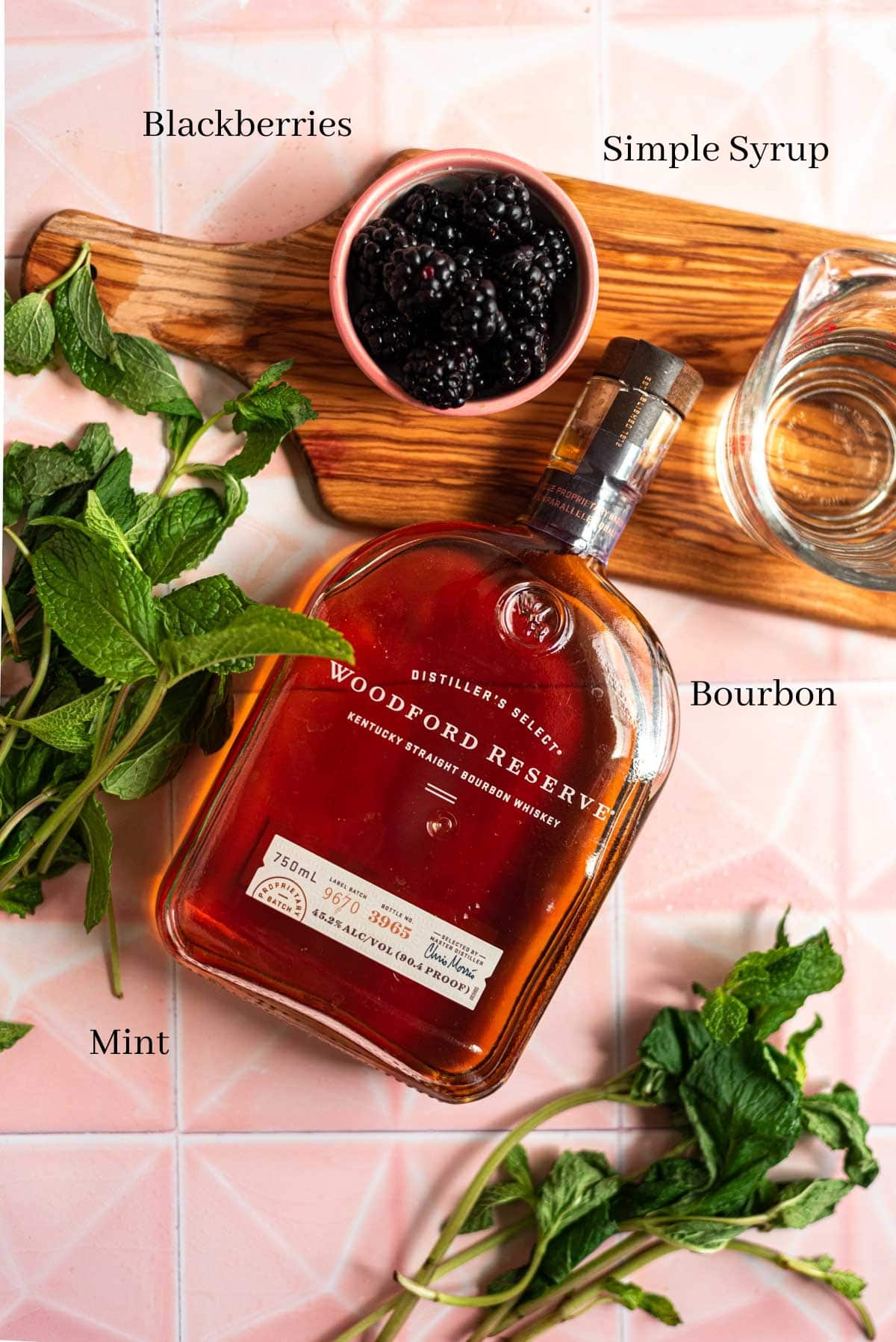 Bourbon, simple syrup, blackberries, and mint on a pink tile table.