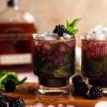 Blackberry mint julep in a textured glass on a wood cutting board with blackberries and mint.