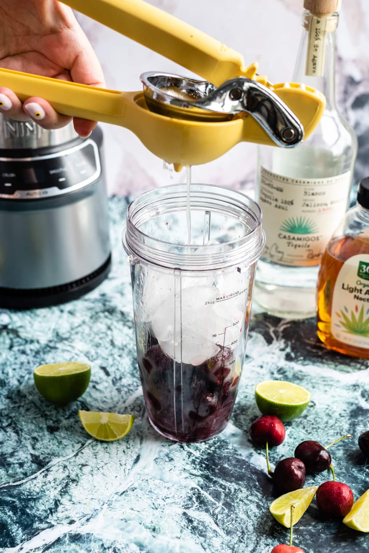 Lime juice being squeezed into a blender filled with ice and cherries.