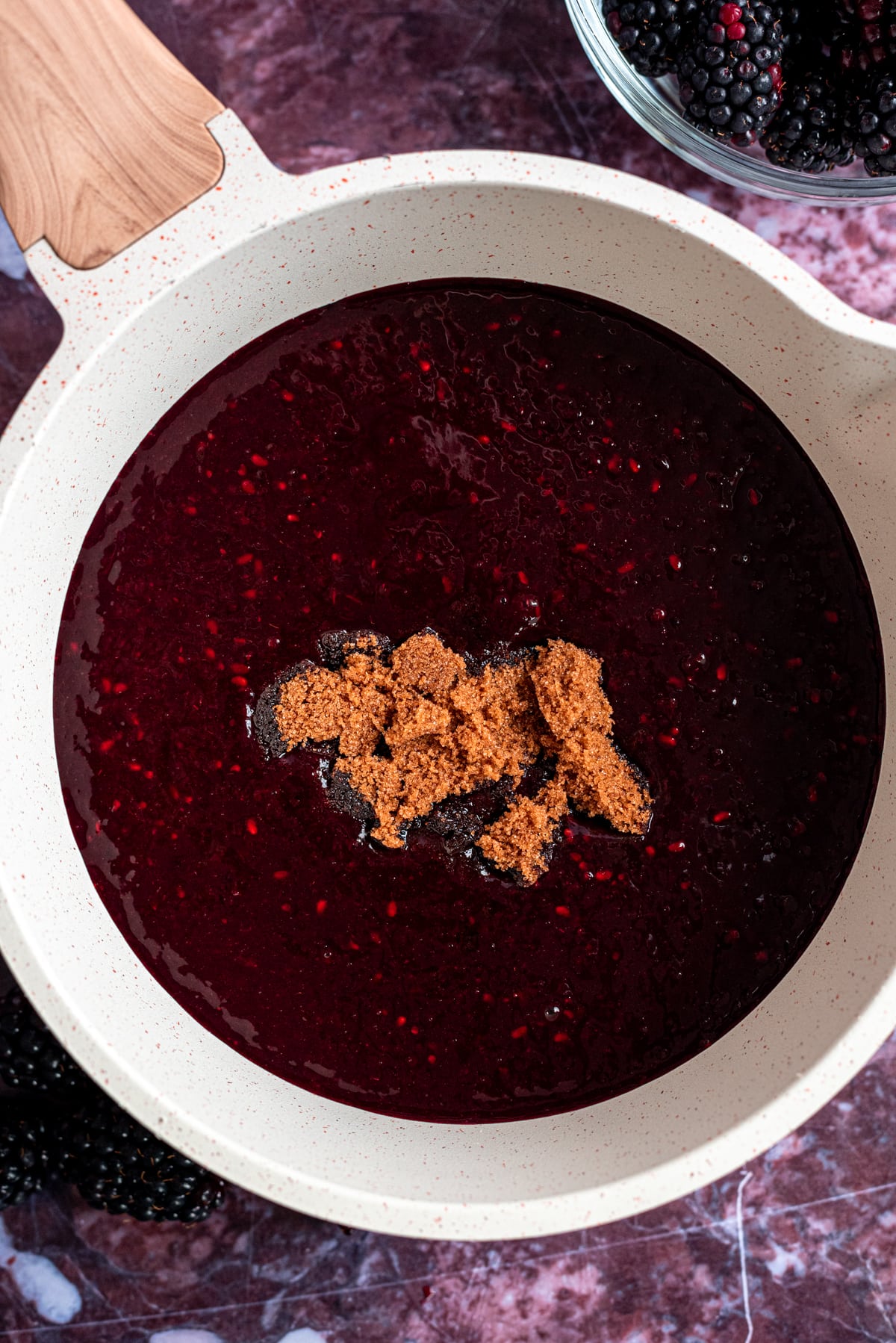The pureed blackberries in a small white pot with the brown sugar setting on top.