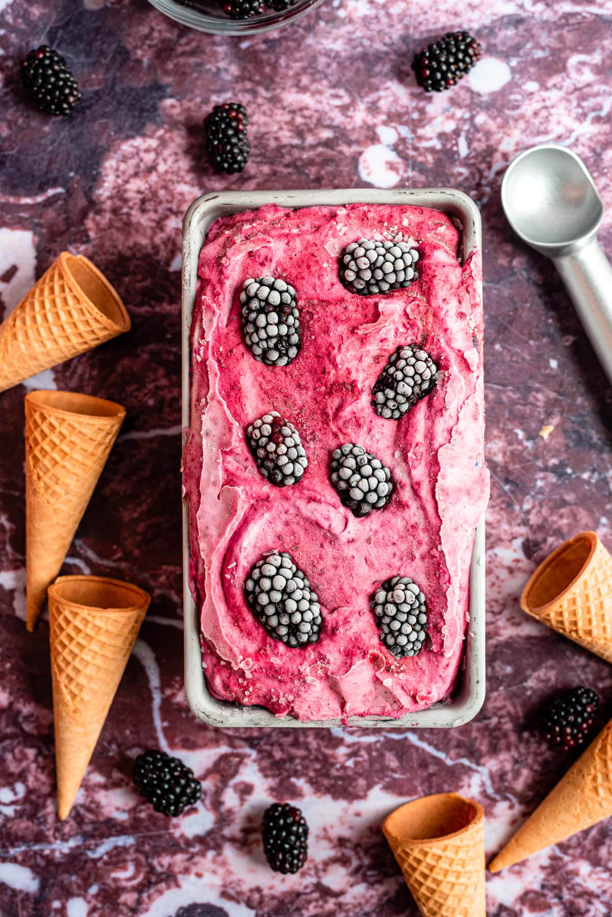 The frozen blackberry ice cream right out of the freezer with ice cream cones on both sides.