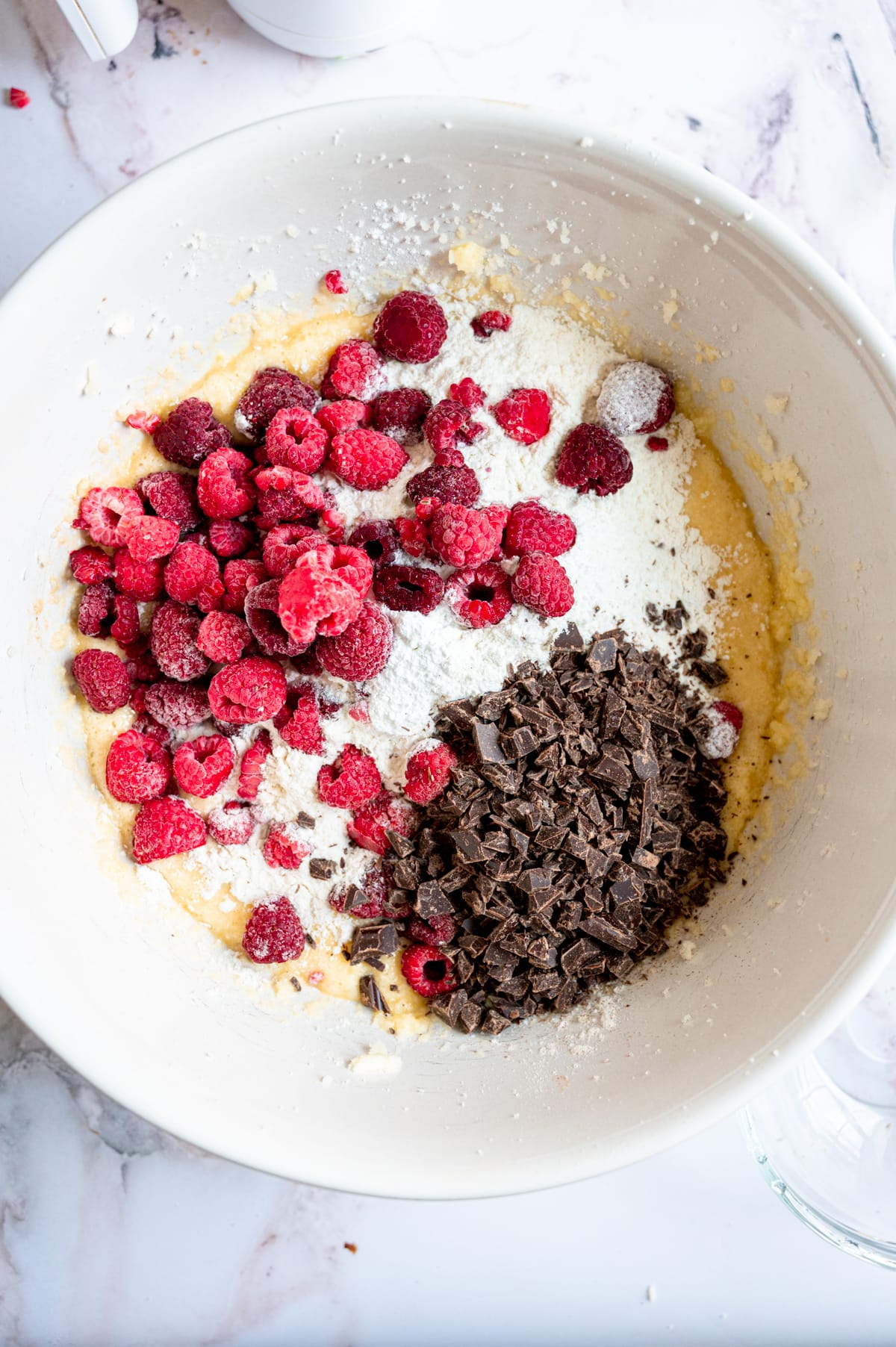 All the ingredients in the mixing bowl with the raspberries and chocolate on top.