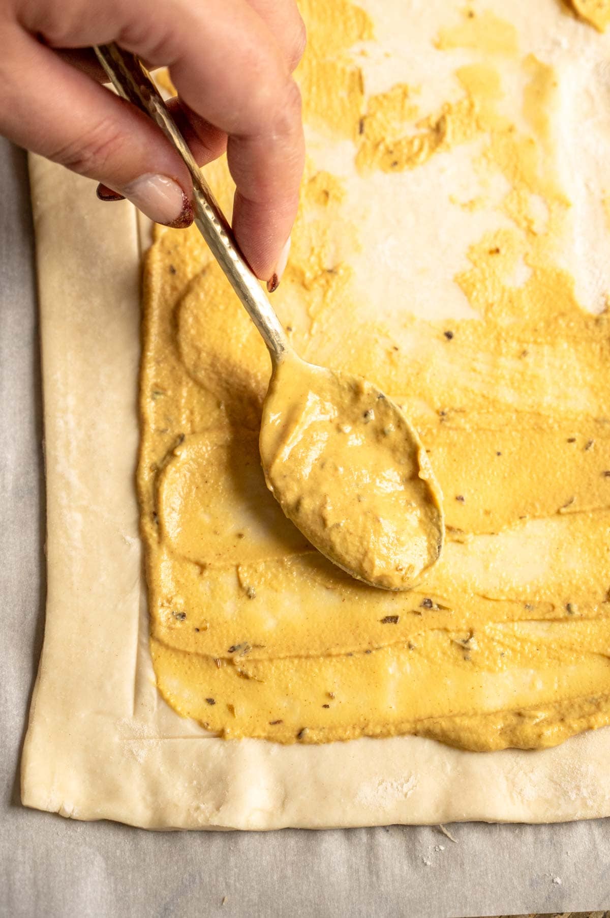 A spoon is spreading the mustard over the puff pastry.