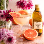 Grapefruit olive oil martini in a curved martini glass surrounded by grapefruit halves.
