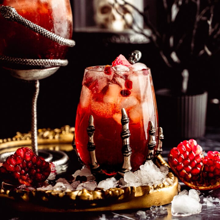 A red cocktail in a skeleton glass on a mirrored tray with a black background.