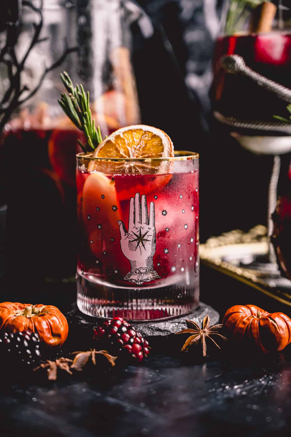 Halloween sangria in a witchy old fashioned glass garnished with a dried orange slice and rosemary.