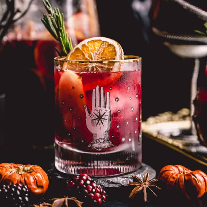 Halloween sangria in a witchy old fashioned glass garnished with a dried orange slice and rosemary.