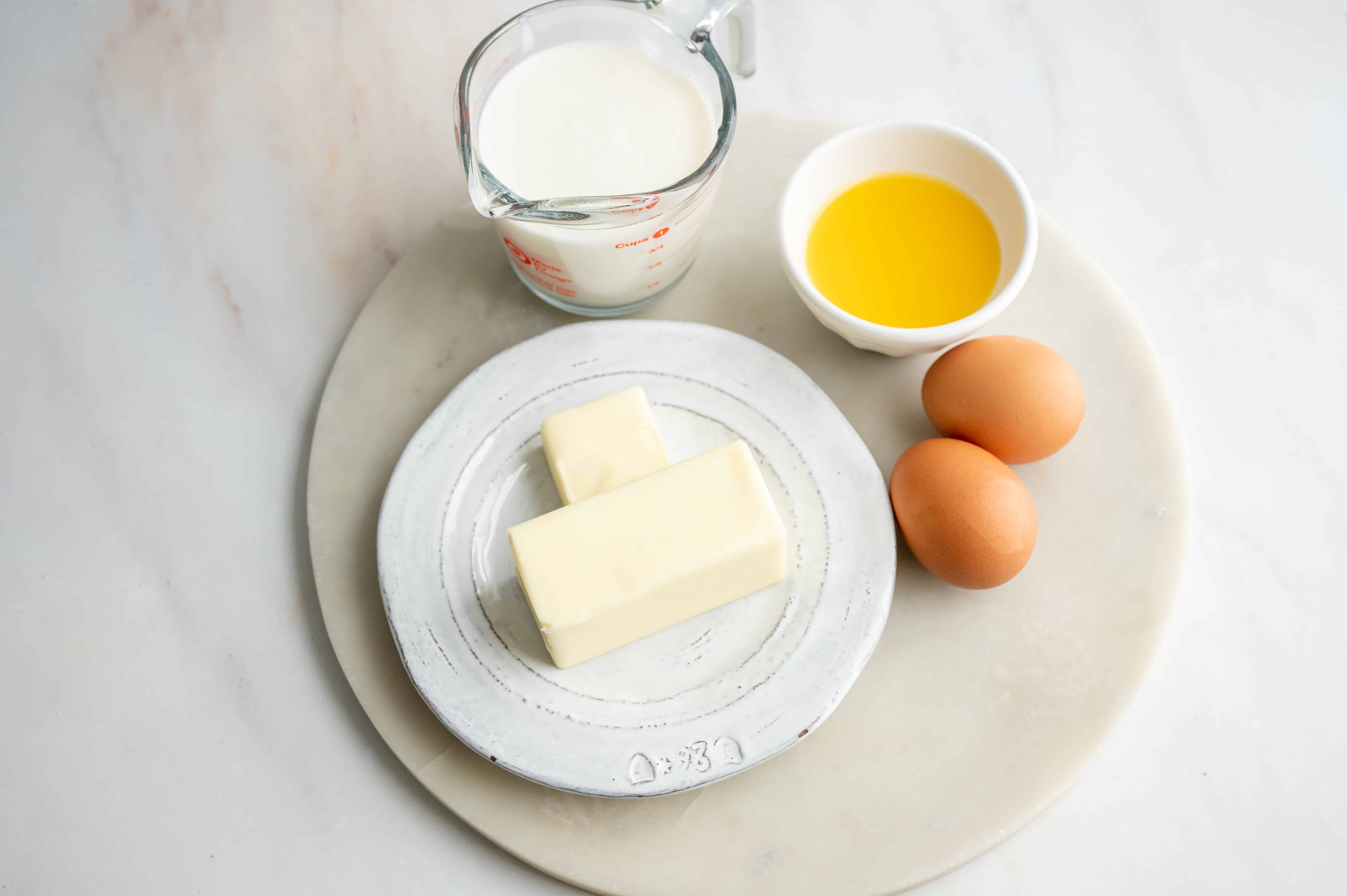 Milk, butter, orange juice and eggs sitting on a marble slab on a table.