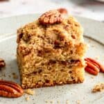 A slice of coffee cake on a speckled plate with a few pecans.