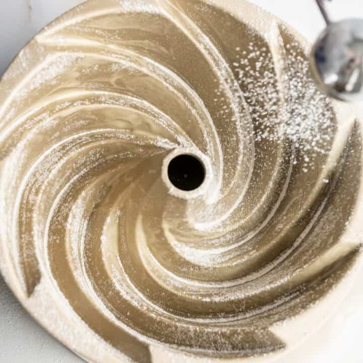 Flour being dusted into a greased bundt pan.