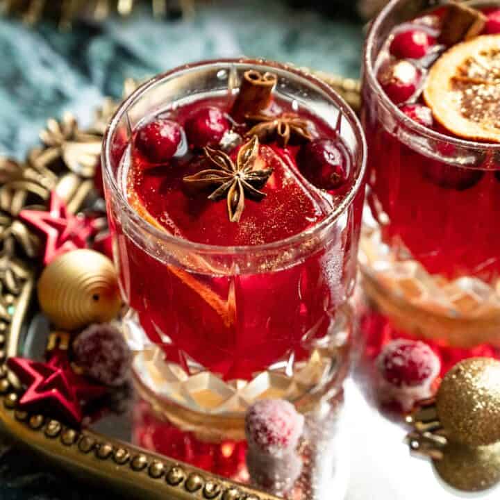 Two cranberry old fashioned on a mirrored tray with mini ornaments.