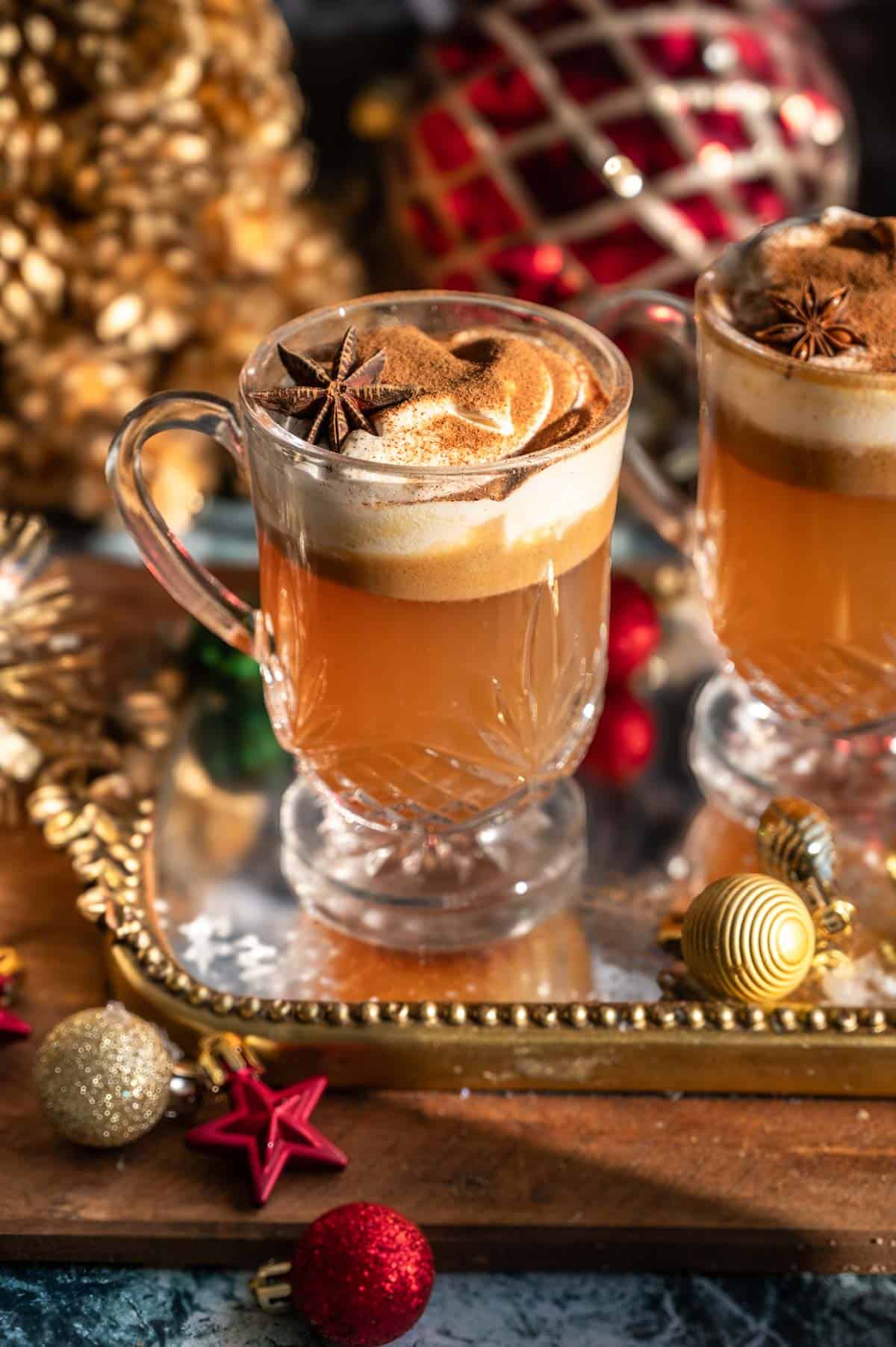 Two glasses of hot buttered bourbon on a mirrored tray and surrounded by ornaments. 
