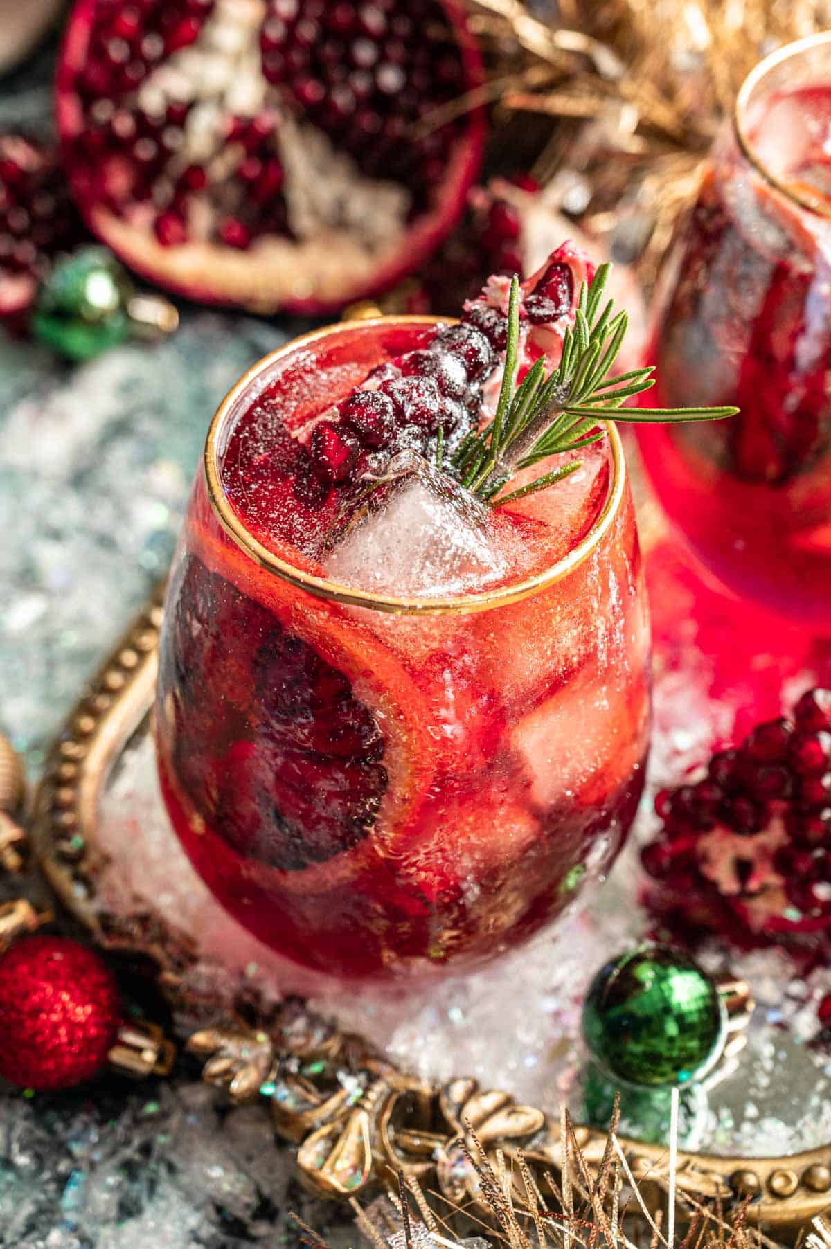 A pomegranate Aperol spritz on a mirrored tray and surrounded by ornaments.