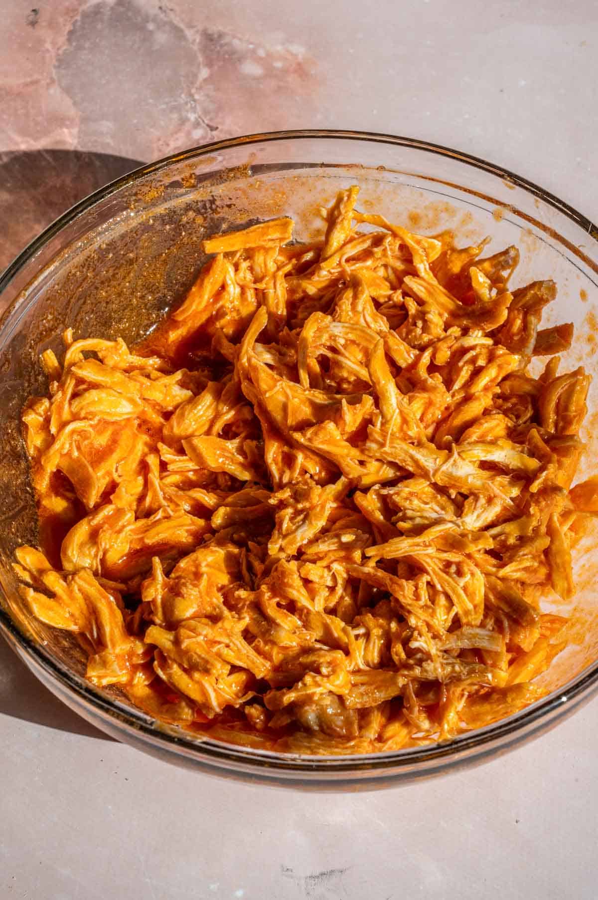 The chicken tossed with the buffalo sauce in a glass bowl.