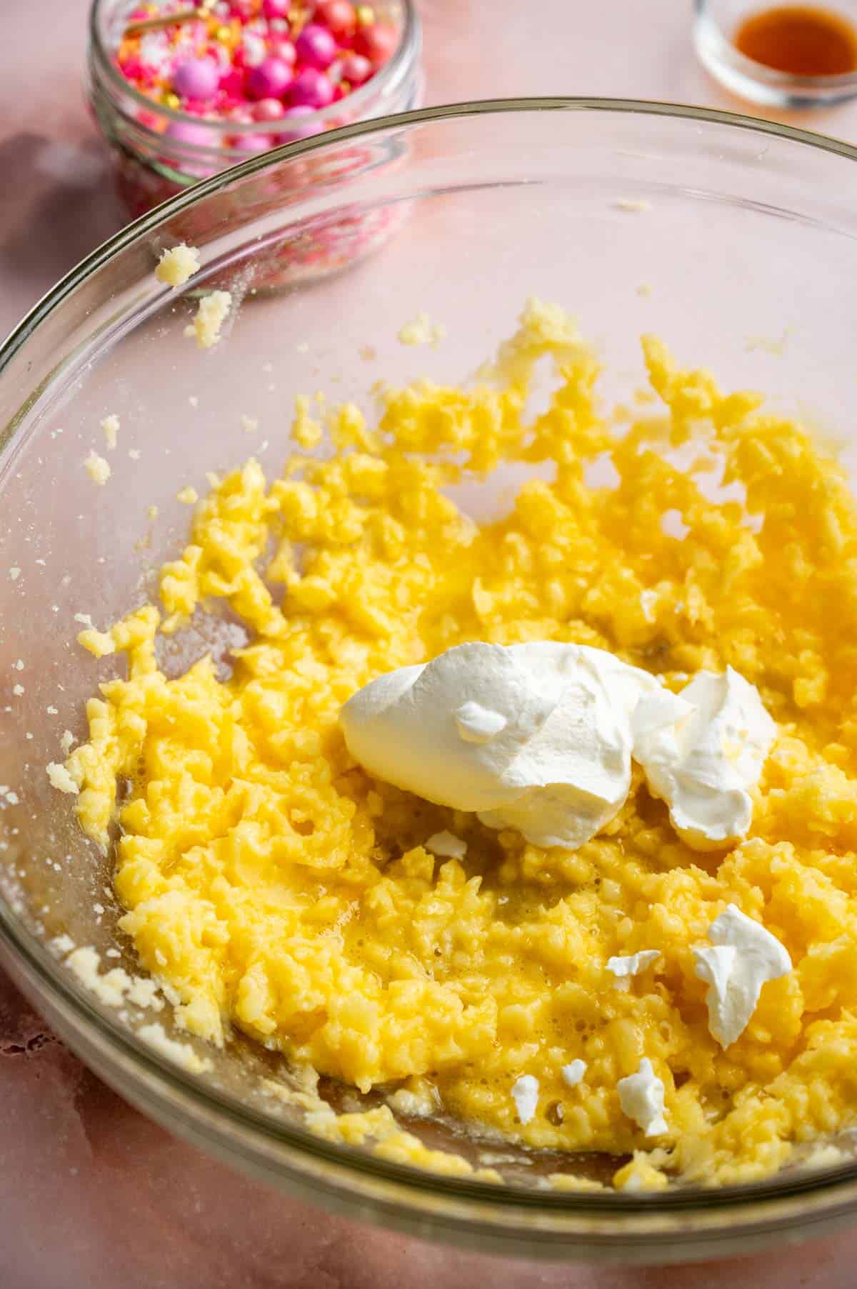 a dollop of sour cream sitting in a glass bowl with the beaten eggs, sugar, and butter.