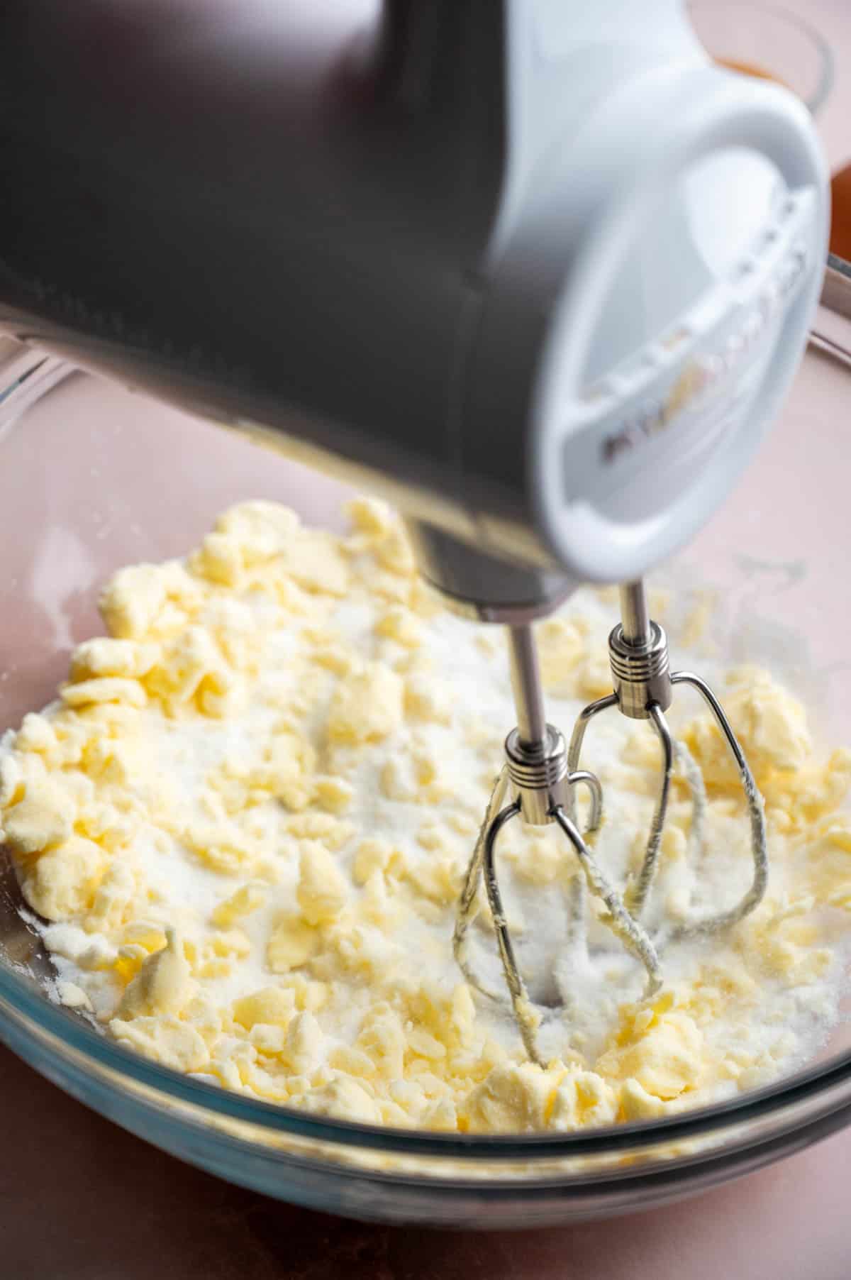 An electric mixer beating butter and sugar and in a glass bowl.