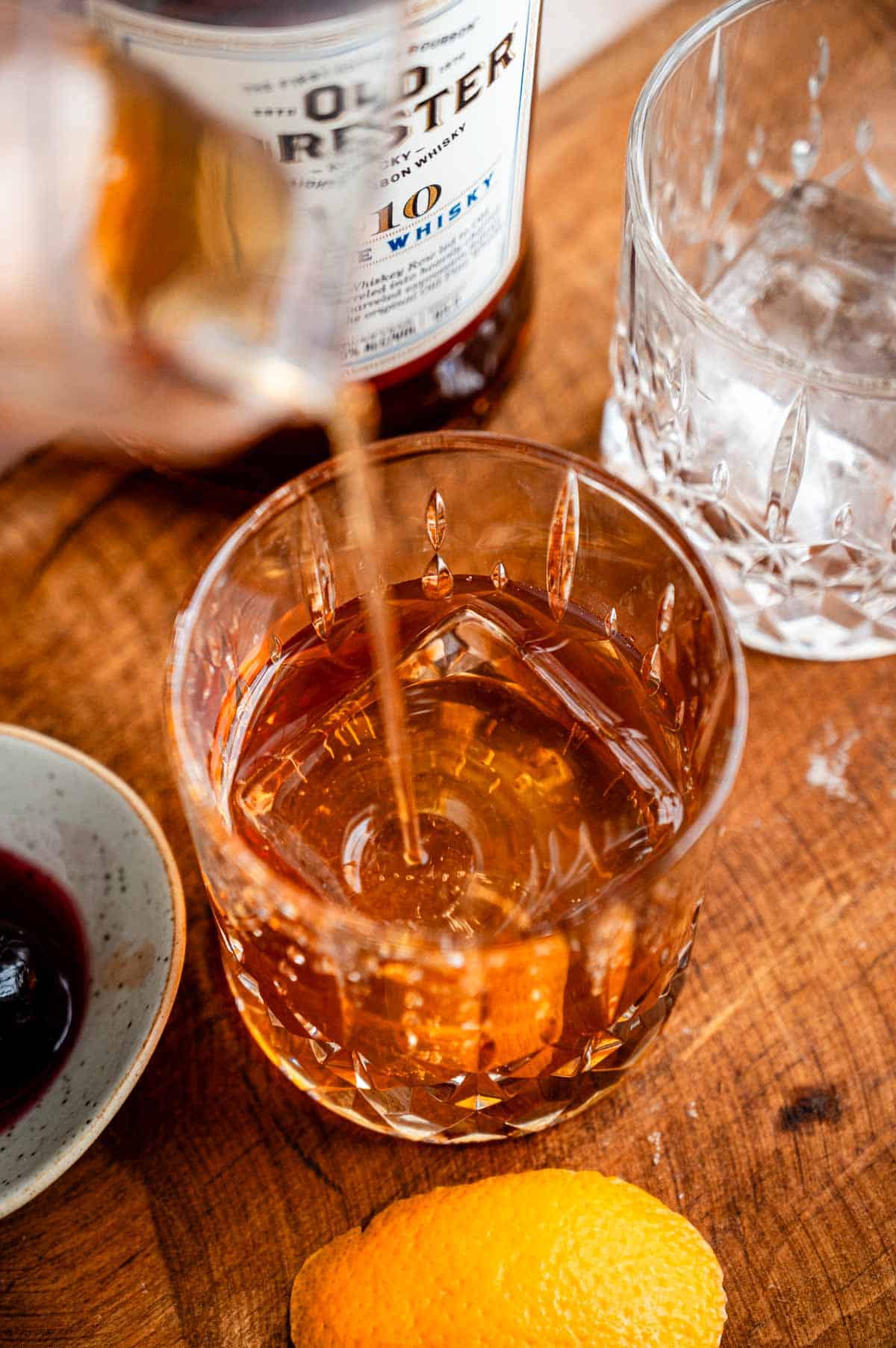 The cocktail being strained into an old fashioned glass with a large ice cube.