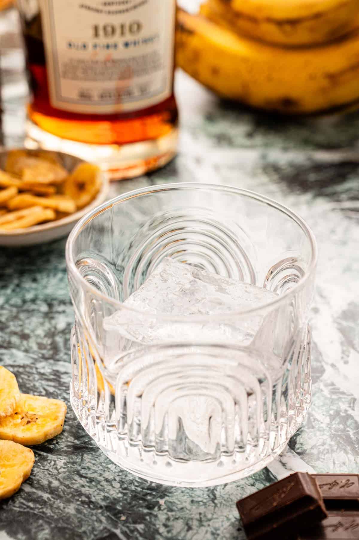 A large ice cube sitting in a rocks glass on a marble table.