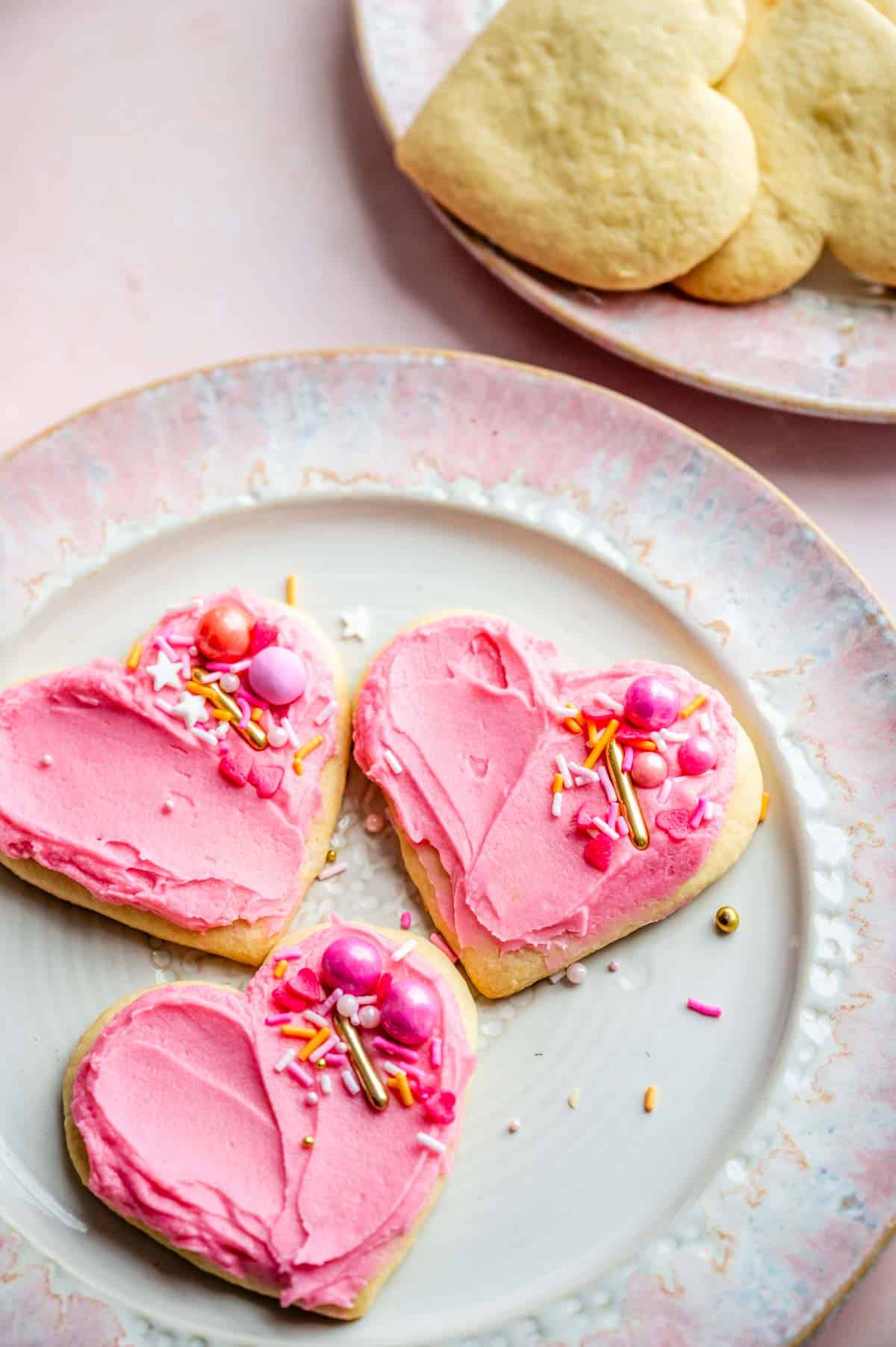 Three frosted cookies sitting on a plate that is on a pink marble table.