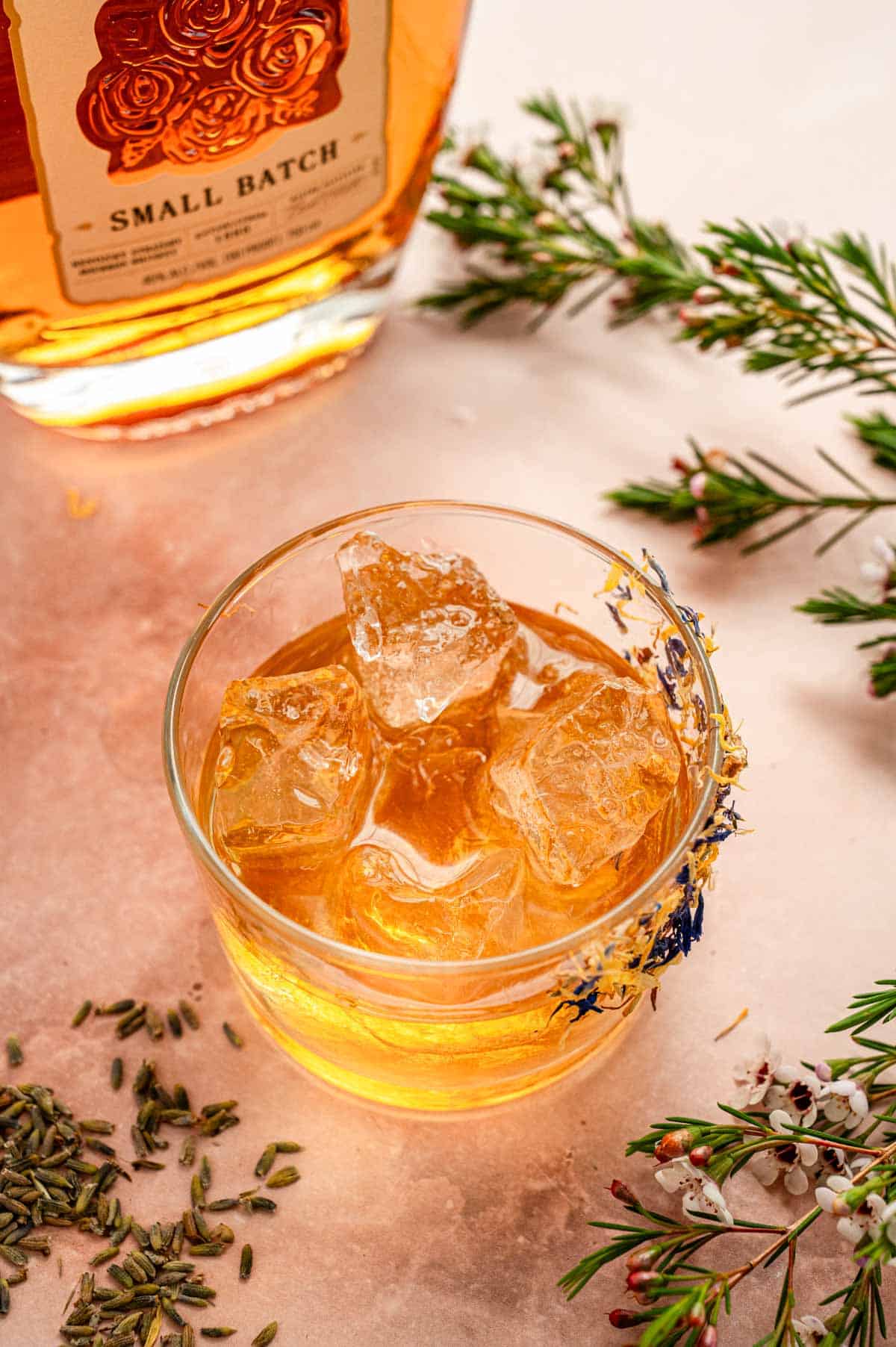 A rocks glass filled with ice, bourbon, and lavender syrup.